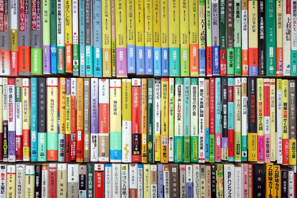 Bookshelf filled with two rows of colorful books, mostly with Japanese titles, arranged vertically and tightly packed together.