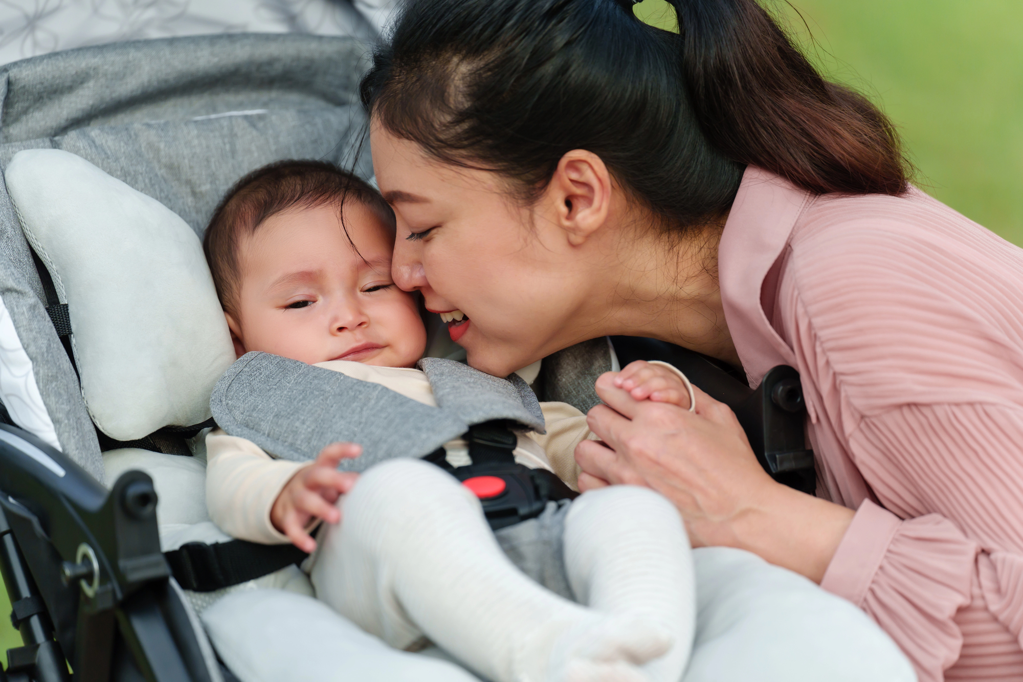 A woman leans in to nuzzle a baby (赤ちゃん, baby in Japanese) seated in a stroller (known as bebii kaa/baby car in Japanese) while holding the baby's hand.