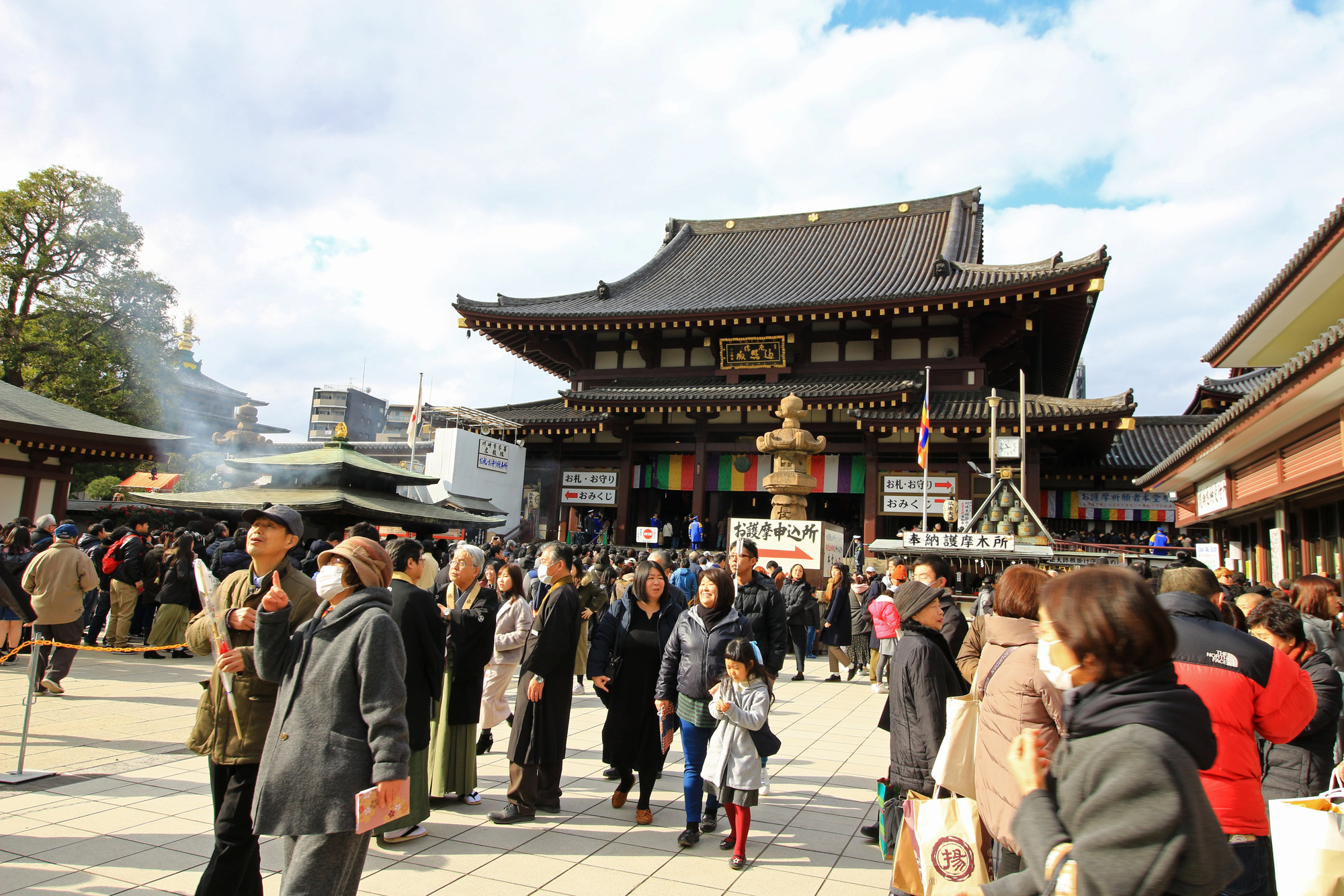 Crowd of people walking and standing in front of a large traditional Japanese shrine on a sunny day, celebrating New Year's Day with the first shrine visit (hatsumode) in Japan in January.