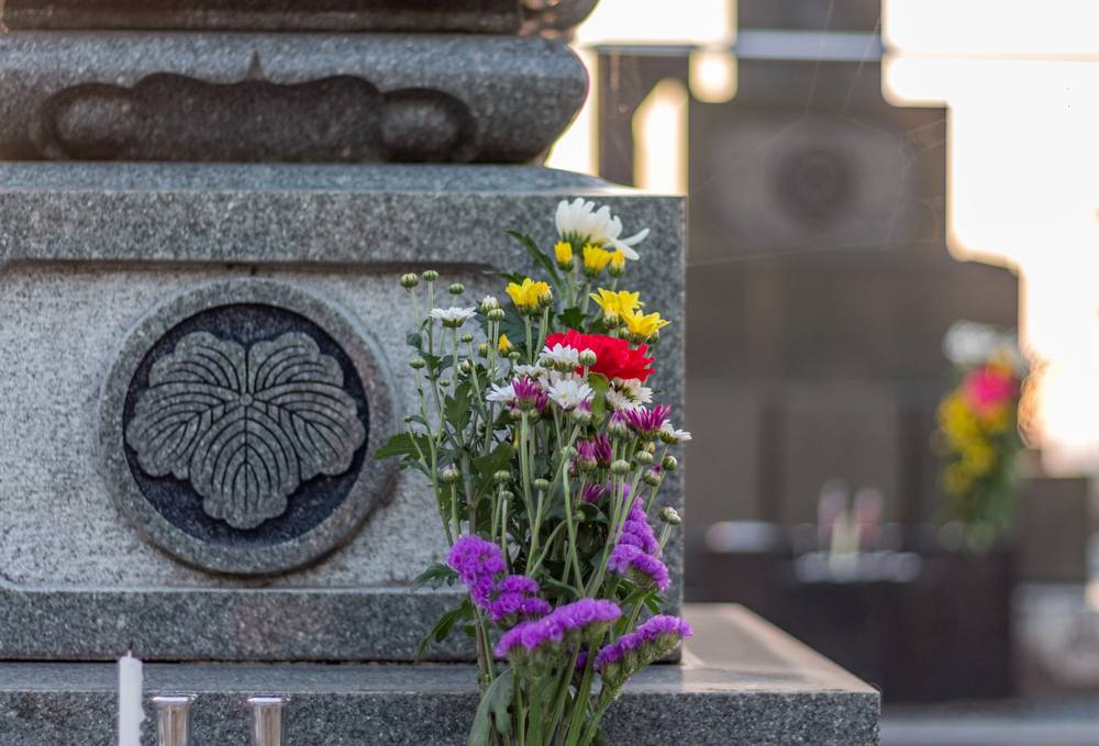 An offering of colorful flowers placed against a stone grave with an engraved crest in a cemetery. Offerings to graves are made during the higan period in March in Japan.