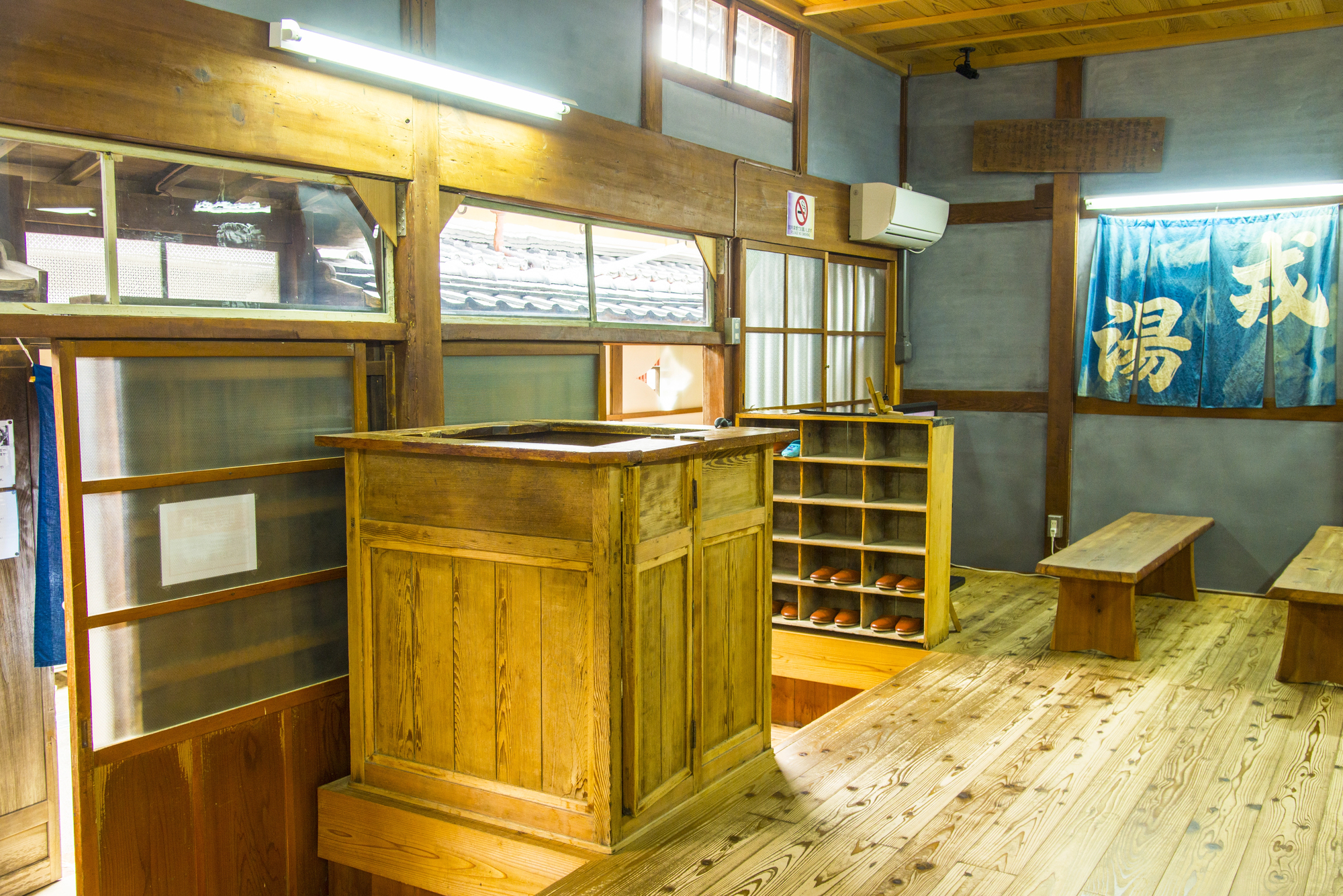 Interior of a traditional Japanese bathhouse with wooden reception counter, shoe cubbies, benches, and blue fabric curtains—an inviting glimpse into how to visit an onsen in Japan.