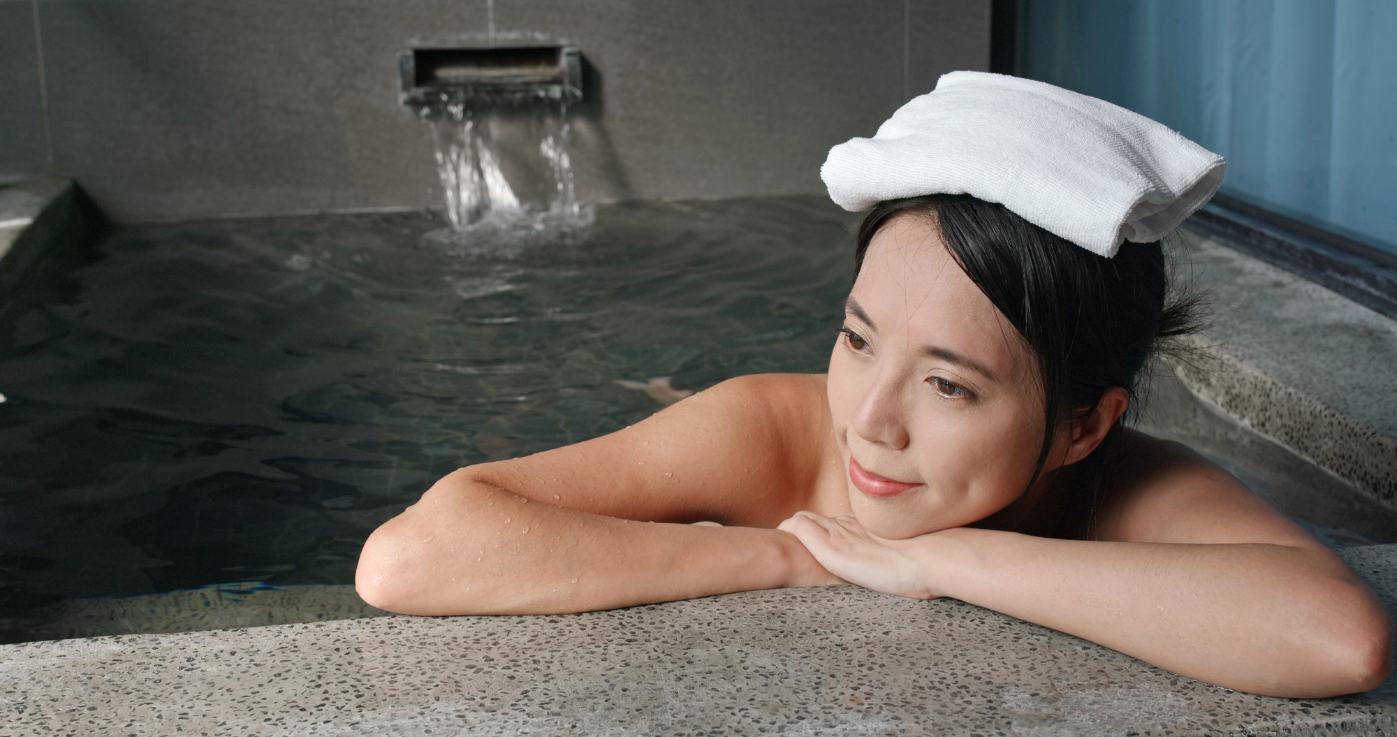 A woman relaxing in a Japanese onsen with a small folded towel balanced on her head.