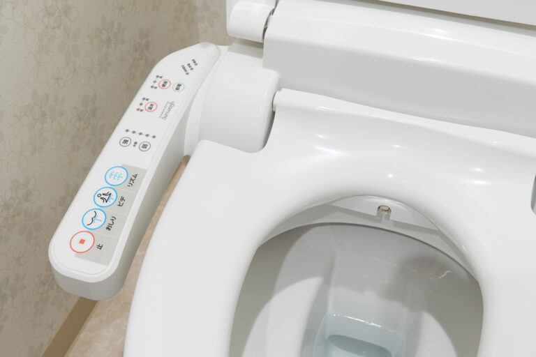 Close-up view of a modern Japanese toilet with an electronic control panel featuring various buttons for bidet and seat functions.
