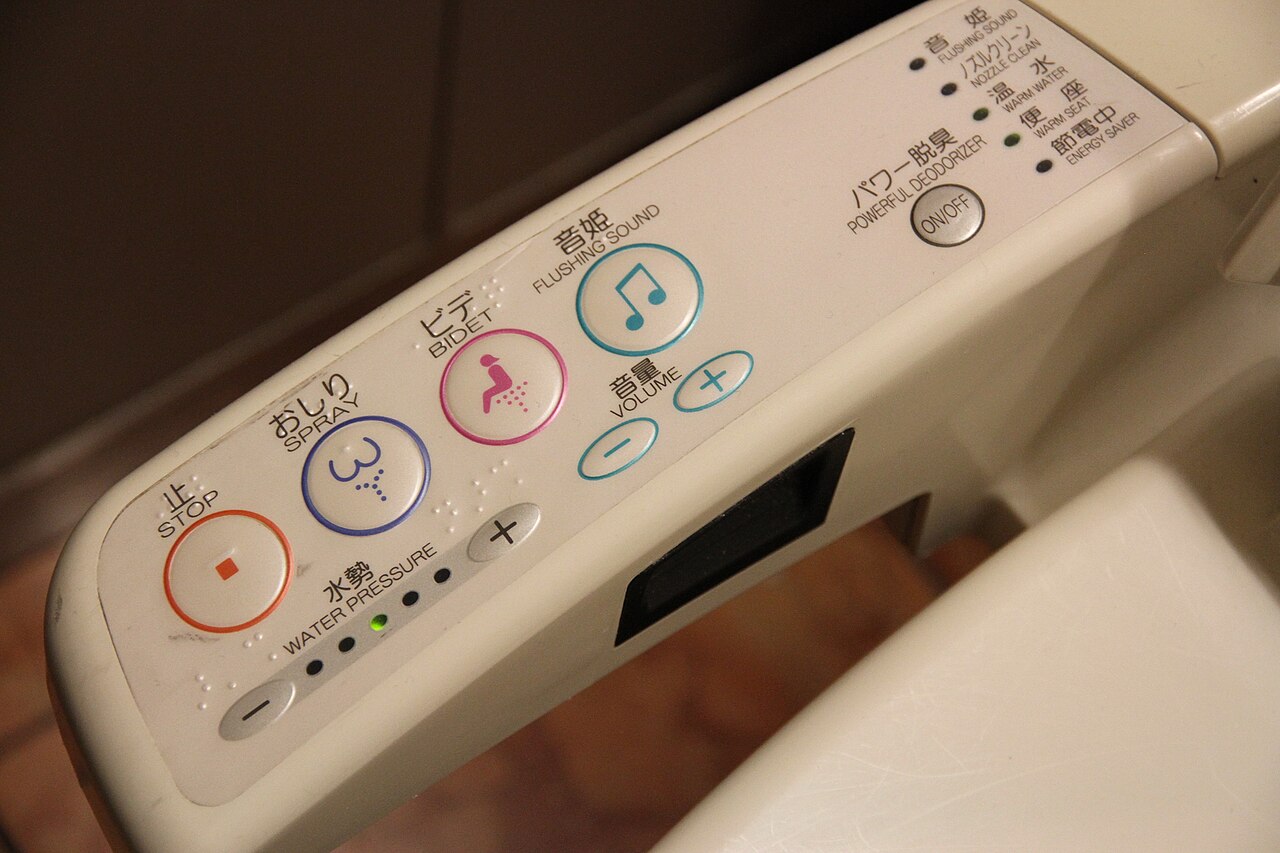 Close-up of an electronic toilet control panel with buttons for stop, spray, bidet, flush sound, volume, water pressure, and power settings—perfect for learning how to use a Japanese toilet. Labels in Japanese and English.