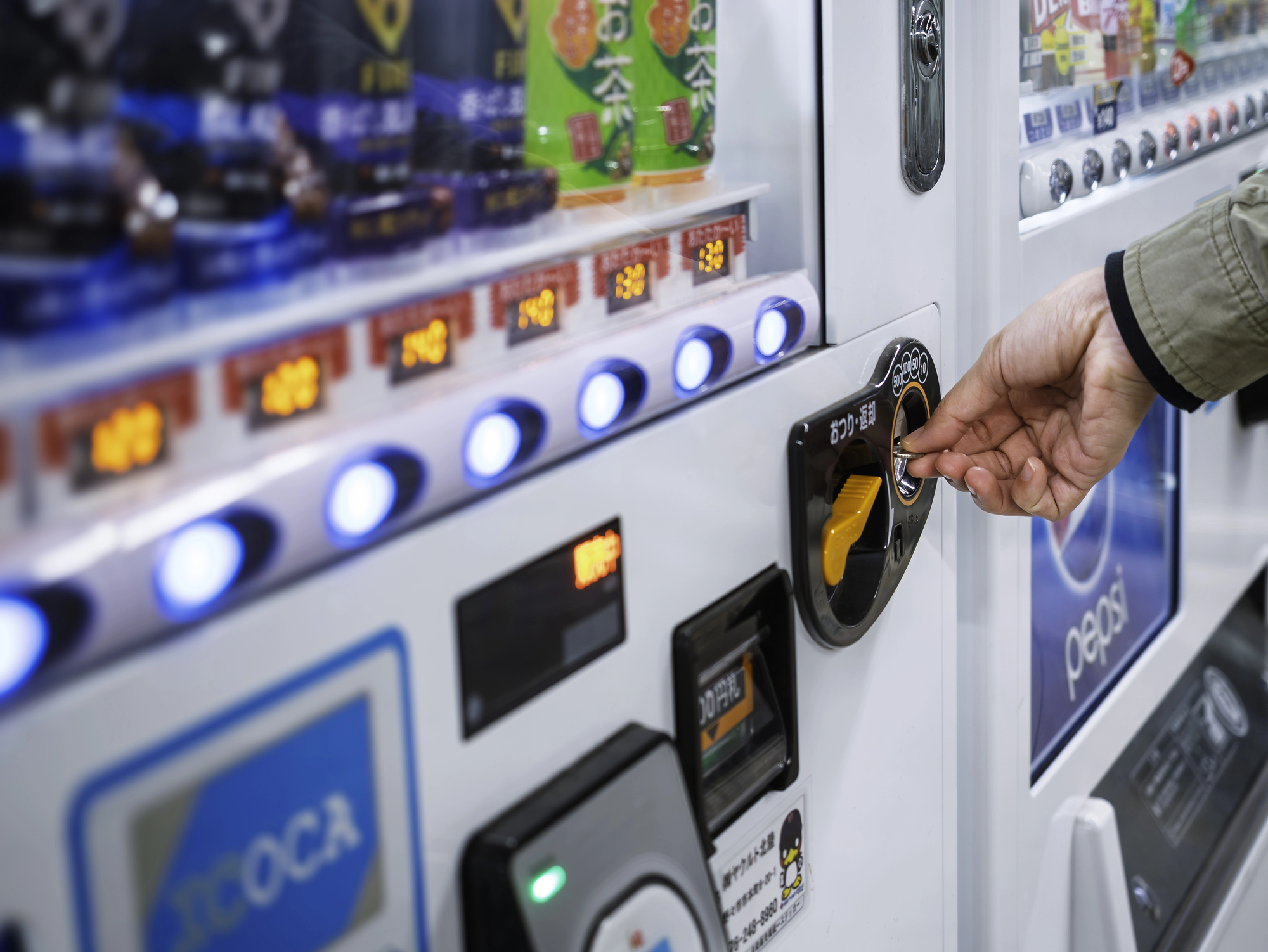 japanese vending machine coin slot A person demonstrates how to use a Japanese vending machine by inserting a coin, with illuminated selection buttons and vending machine instructions visible.