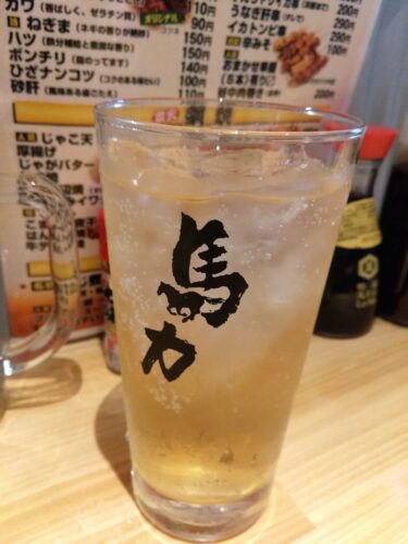 chuuhai izakaya japan A tall glass of a light-colored beverage with ice sits on a wooden table in front of a Japanese menu, capturing the inviting atmosphere of an izakaya you might visit in Japan.