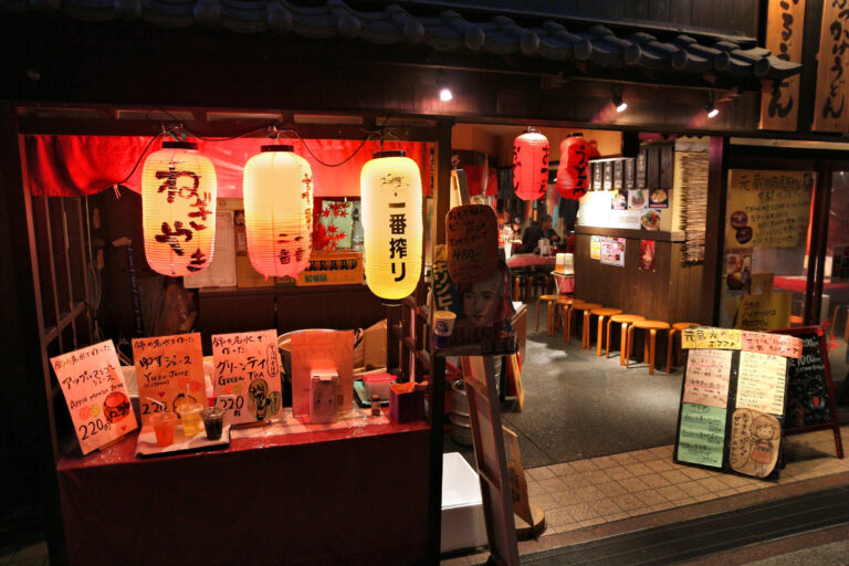 A Japanese Izakaya restaurant with illuminated lanterns and handwritten menu boards displayed at the entrance during nighttime invites you to experience the vibrant nightlife of Japan on your next visit.