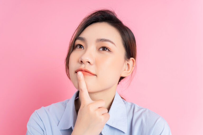Japanese woman looking thoughtful with a finger to her mouth, isolated on a pink background
