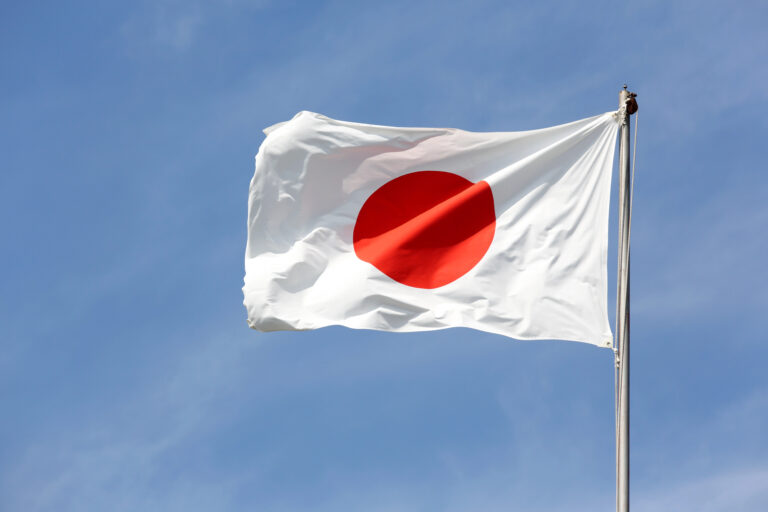 A Japanese flag with a red circle on a white background is flying on a flagpole against a clear blue sky.