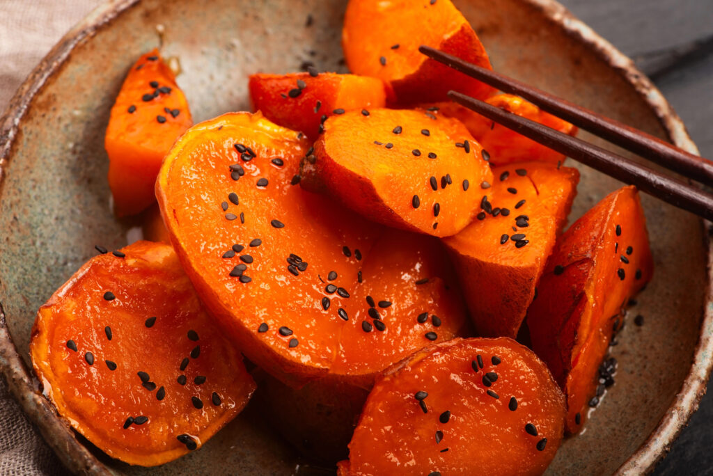 Sliced roasted sweet potatoes with black sesame seeds in a ceramic bowl, with chopsticks on the side—a dish that is popular during September in Japan.