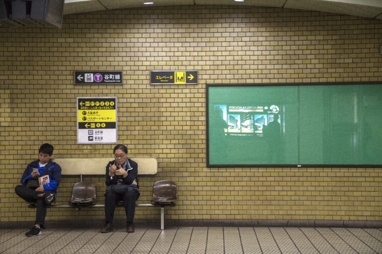 two people waiting on a bench at a train station in Japan