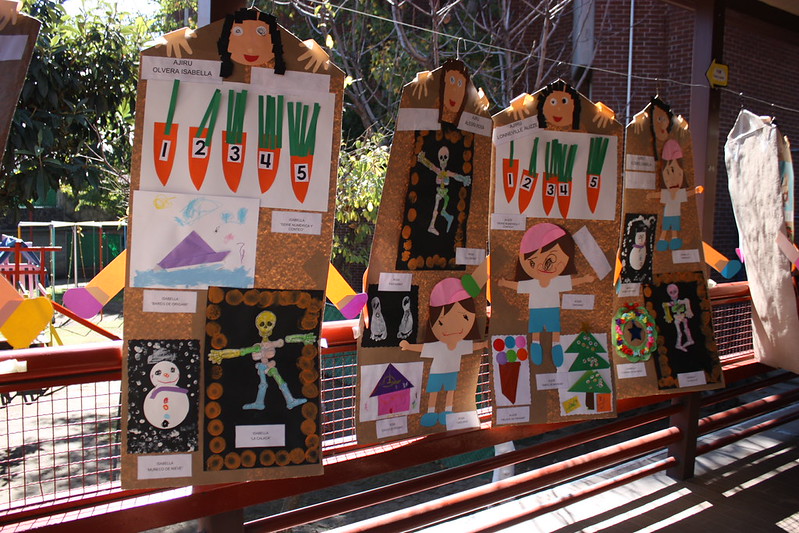Children’s art projects featuring drawings, skeletons, and paper cutouts hang on display outside on a railing in sunlight, typical display at a school bunkasai (culture festival) held in November in Japan.