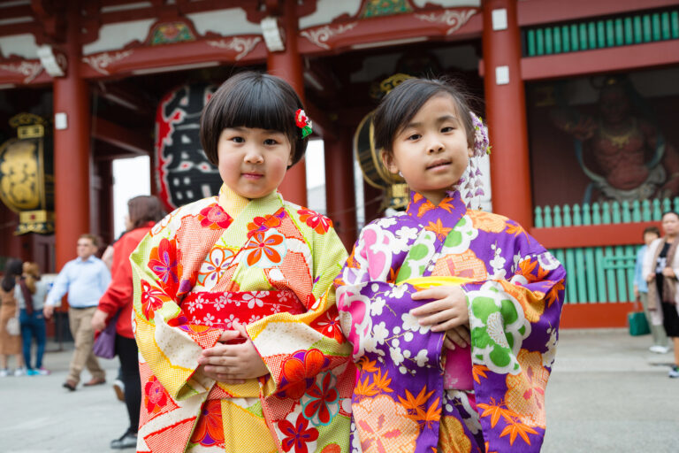 Two young girls in colorful kimonos stand in front of a traditional Japanese temple, dressed for shichi-go-san, an even honouring children which is held in November in Japan.