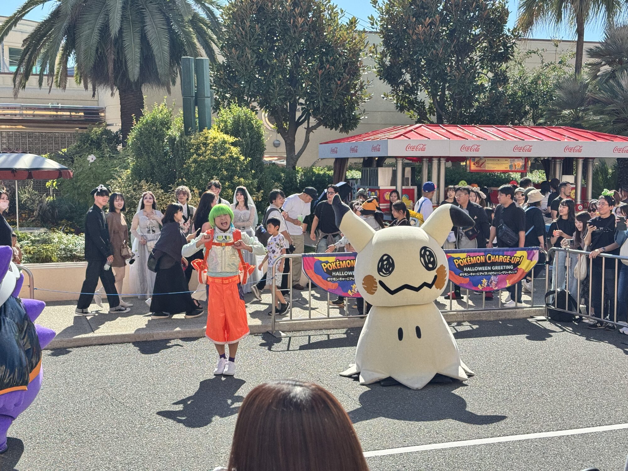People in costumes, including a large Mimikyu character, walk in a Halloween parade at USJ in Japan while spectators watch from behind barriers.
